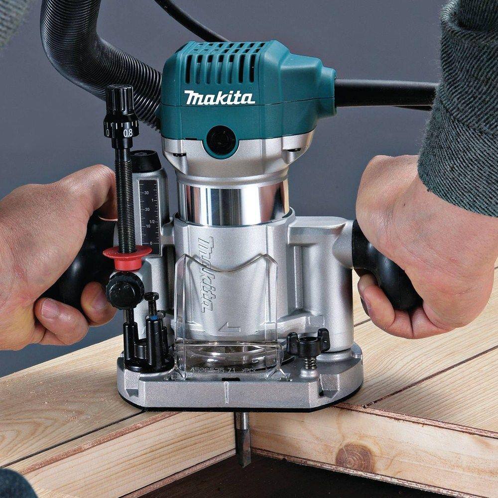 Close-up of hands firmly gripping the Makita RT0701CX7 variable speed compact router in its plunge base, performing a precise plunge cut on a wood workpiece.