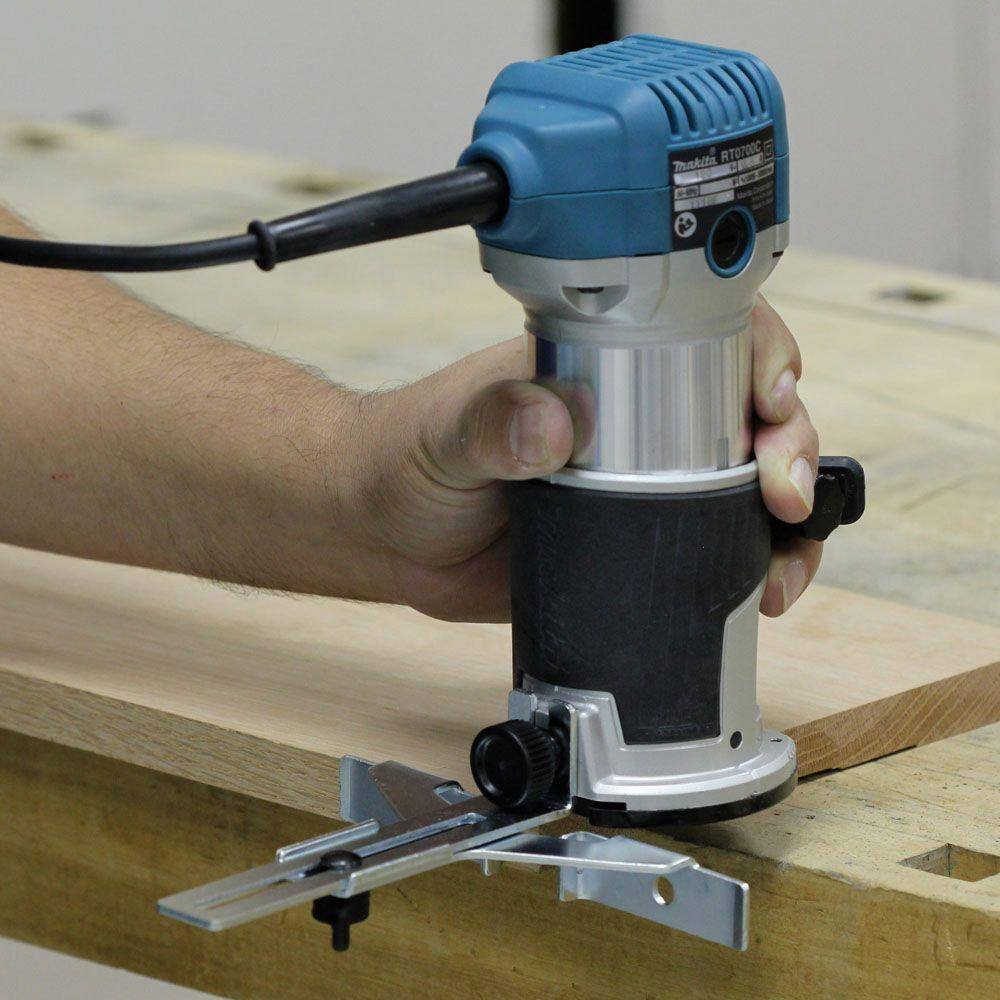 A user guiding the Makita RT0701CX7 6.5 Amp corded compact router equipped with the fixed base and straight guide to accurately shape a board's edge.