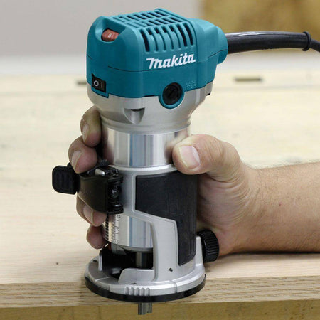 A woodworker securely gripping the Makita RT0701CX7 6.5 Amp compact router in its fixed base for precise edge routing on a wooden board.