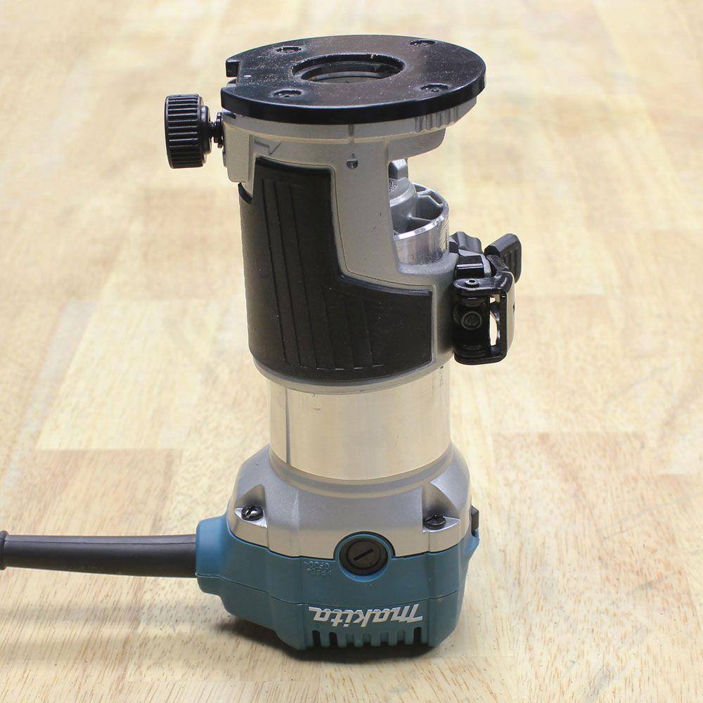 Underside angled view of the Makita compact router showing the non-marring fixed base plate and the heavy-duty aluminum motor housing.