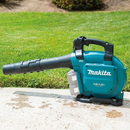 The Makita XBU04Z cordless blower resting on a concrete path next to a lawn. The two empty battery slots are visible, highlighting the X2 (36V) system.
