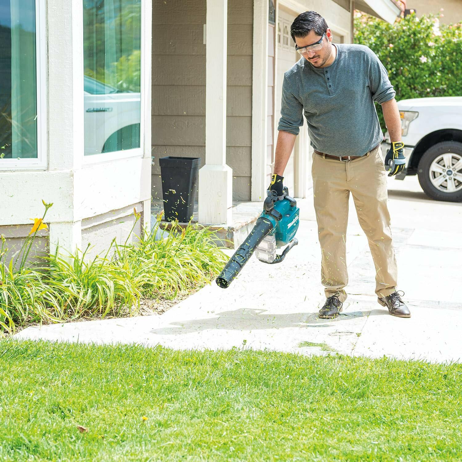 Full shot of a user operating the Makita XBU04Z blower on a residential driveway, wearing safety glasses and directing the airflow to clear grass clippings from the concrete.