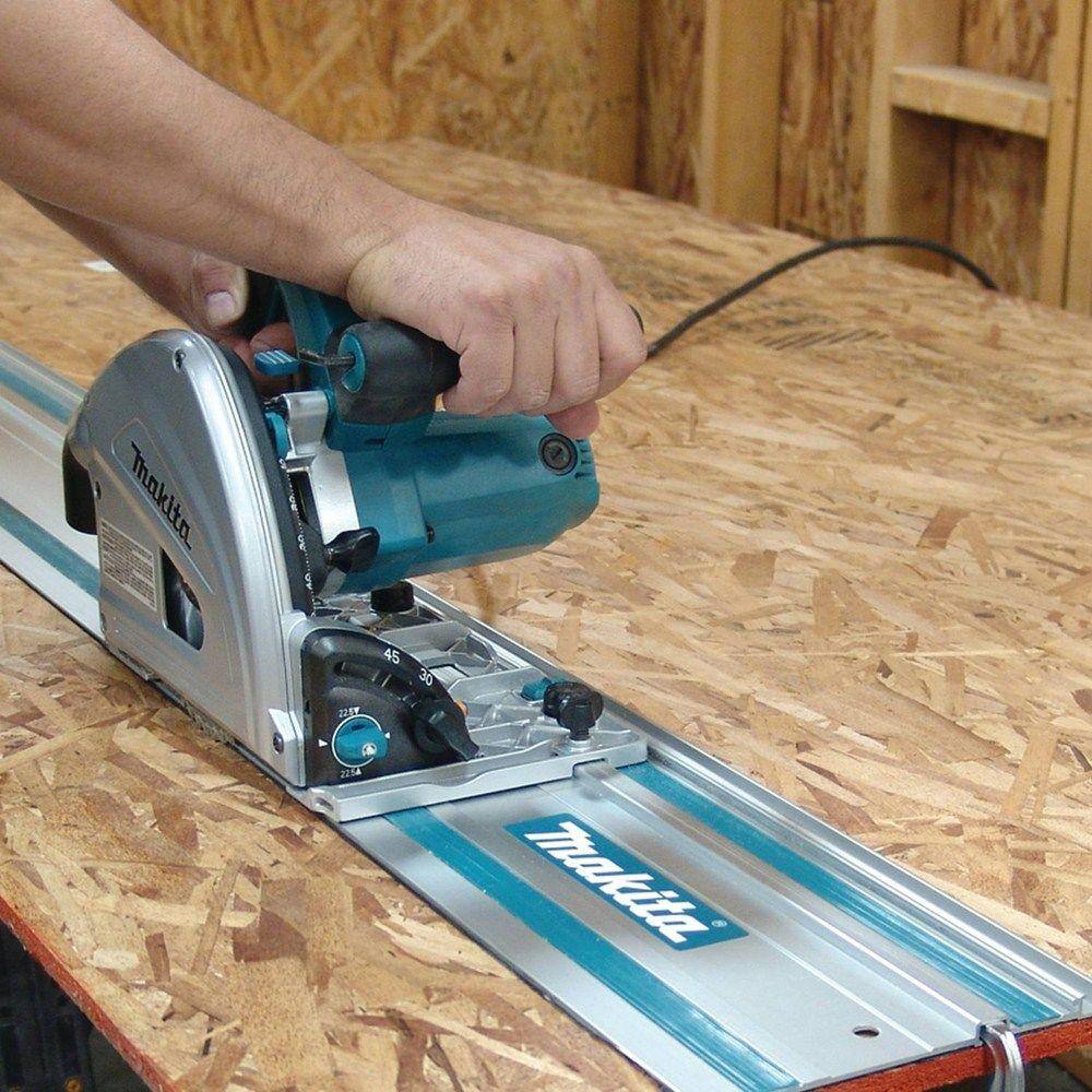 Action shot of a professional craftsman using the Makita SP6000J1 plunge saw and guide rail track to perform a high-precision rip cut on a large wooden panel, highlighting the tool's splinter-free mirror finish capability.