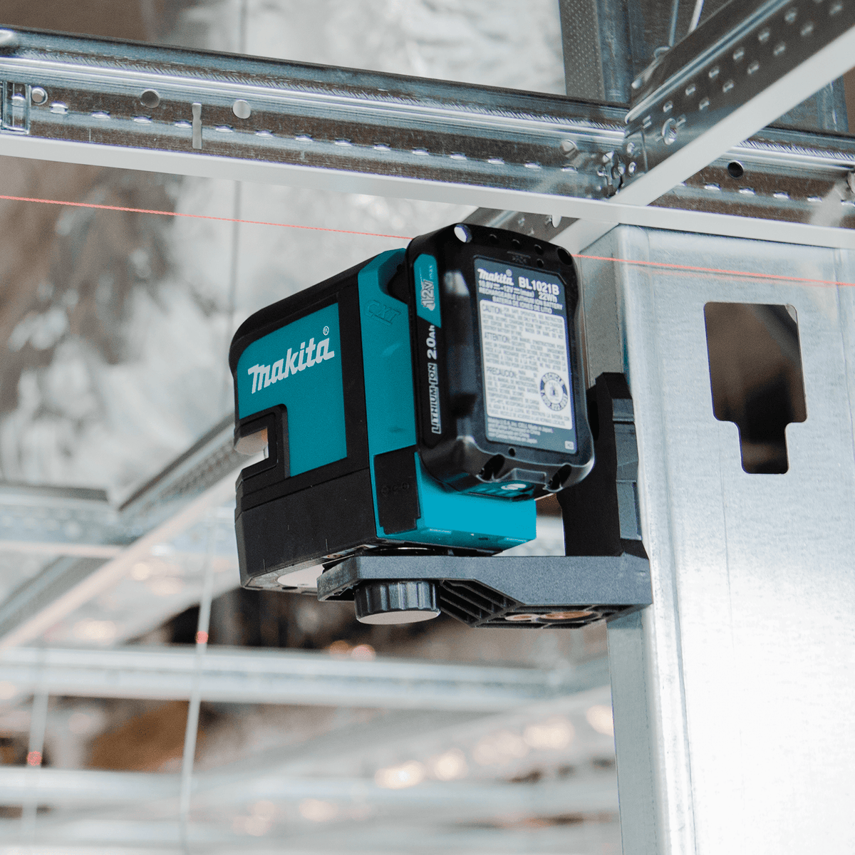 Makita SK105D cross-line laser magnetically attached to a commercial steel stud projecting a red datum line for drywall track layout.