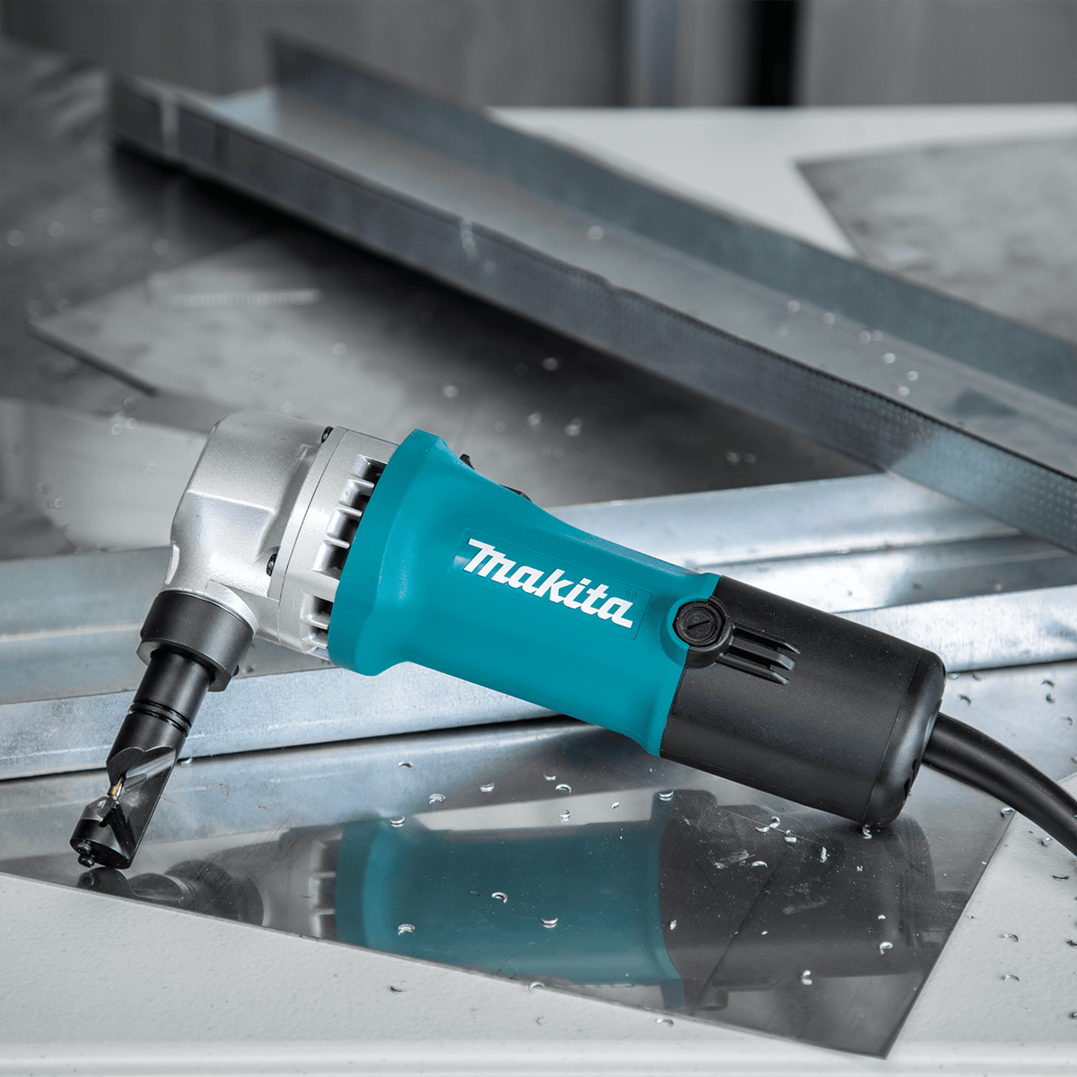 Makita JN1601 corded sheet metal nibbler resting on a metal workpiece surrounded by clean, burr-free punch chips.