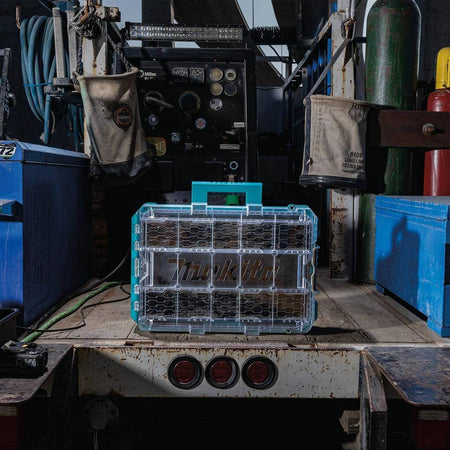Wide action shot of the Makita MAKTRAK Deep Medium Organizer resting on a jobsite work truck, demonstrating its rugged impact-resistant body and high-visibility clear lid in an industrial environment.