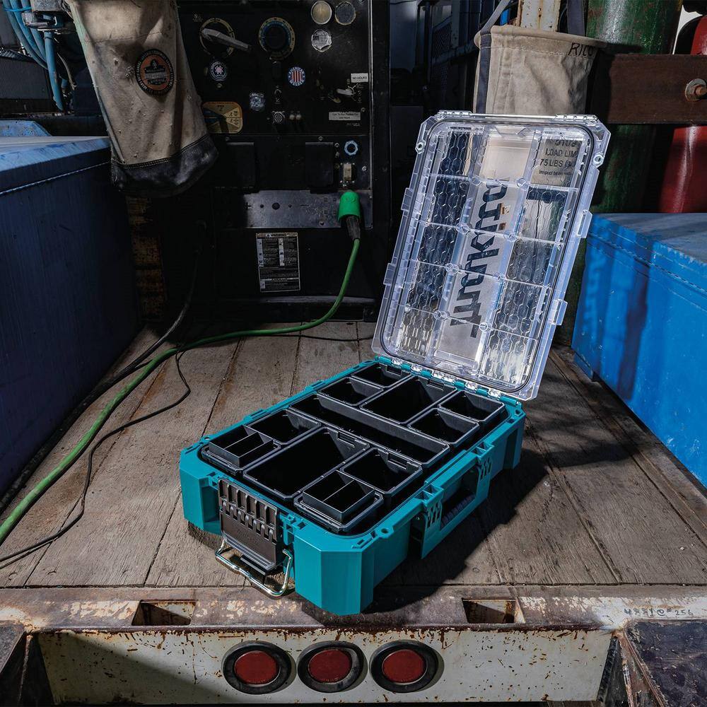 The Makita T-90043 modular storage box with the lid fully open in a workshop setting, showcasing the versatile interior layout and deep bins designed for professional tool and hardware organization.
