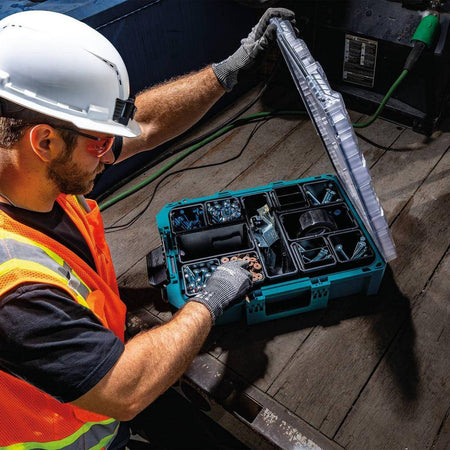 A worker wearing safety gear reaches into the Makita MAKTRAK Deep Medium Organizer, showcasing the deep 5-inch bins that provide high-volume storage for bulk screws and fasteners.