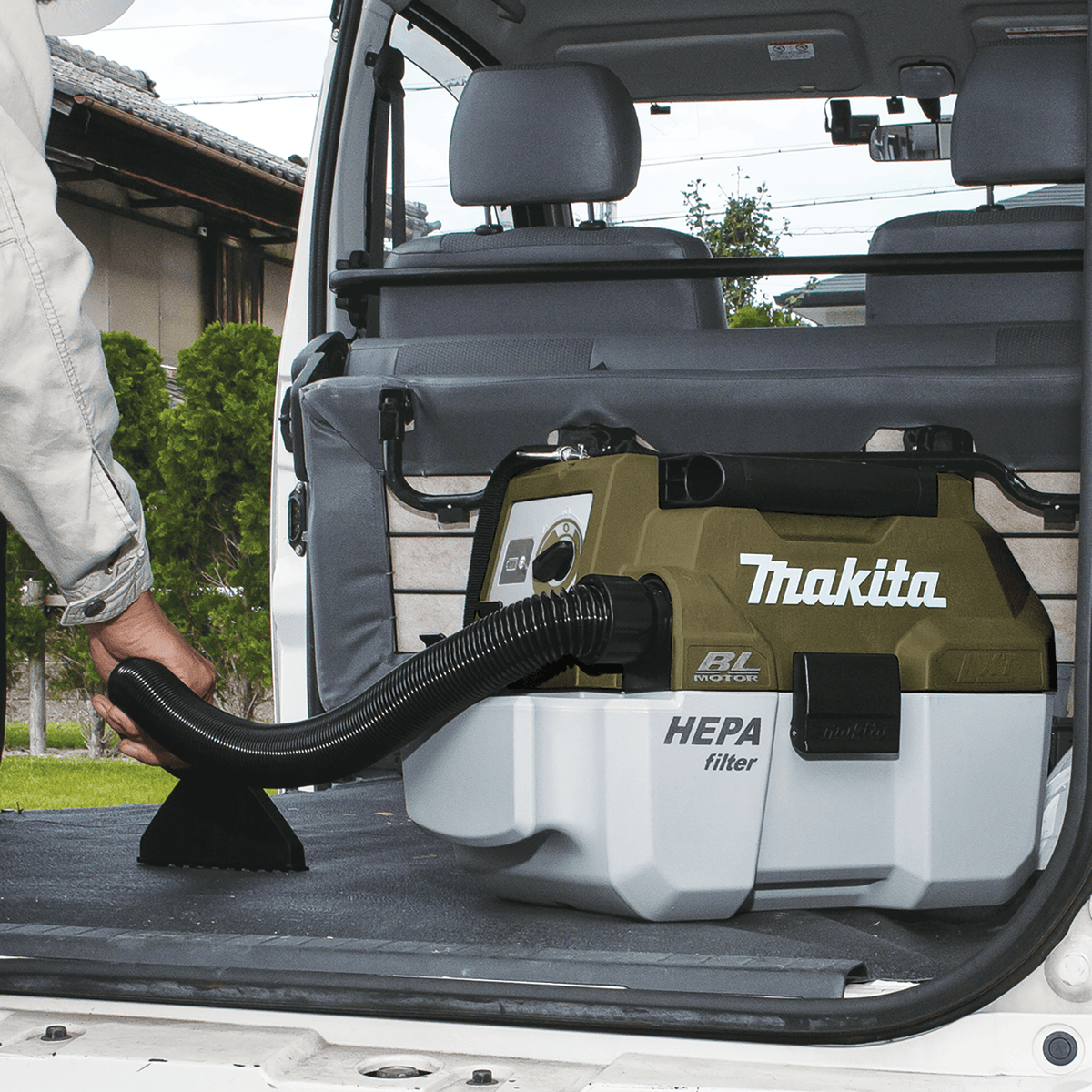 Worker using the wide upholstery nozzle on the Makita ADCV11Z 18V vacuum to clean the cargo liner of a utility van.