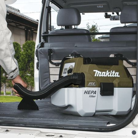 Worker using the wide upholstery nozzle on the Makita ADCV11Z 18V vacuum to clean the cargo liner of a utility van.