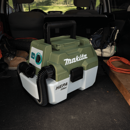 Makita ADCV11Z 18V LXT wet dry canister vacuum stowed neatly inside a SUV trunk next to outdoor and camping equipment.