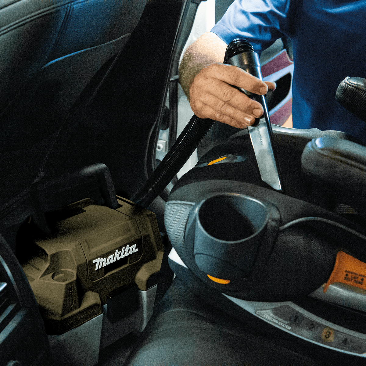 Detailer using the crevice tool attachment on the Makita ADCV11Z cordless vacuum to clean tight seams in a car seat.
