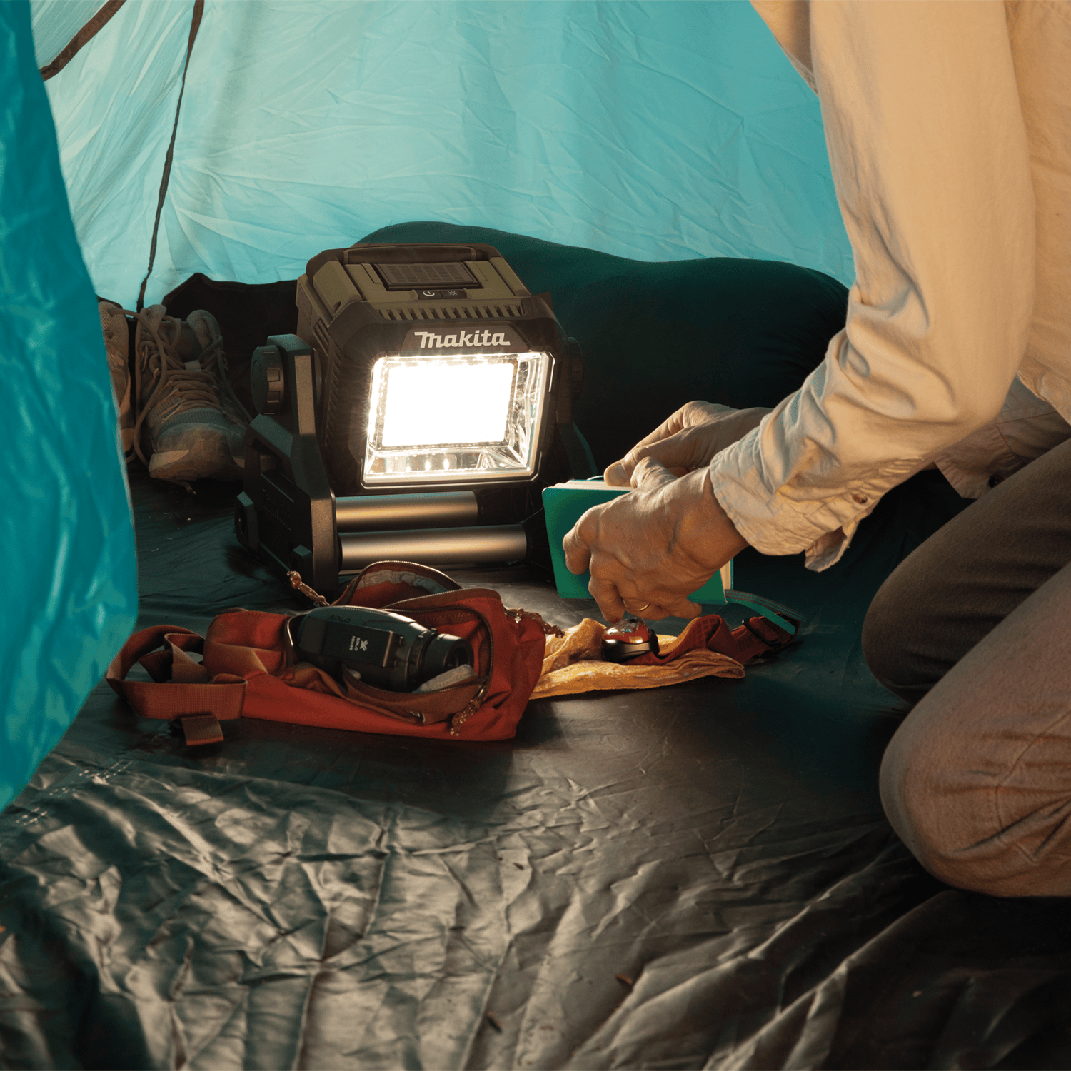 Camper using the Makita ADML811 18V LED floodlight inside a camping tent to provide 3,000 lumens of wide-angle ambient illumination.