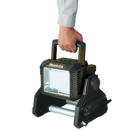 Person carrying the 10.4-pound Makita ADML811 18V LED area floodlight using its ergonomic folding top transport handle.