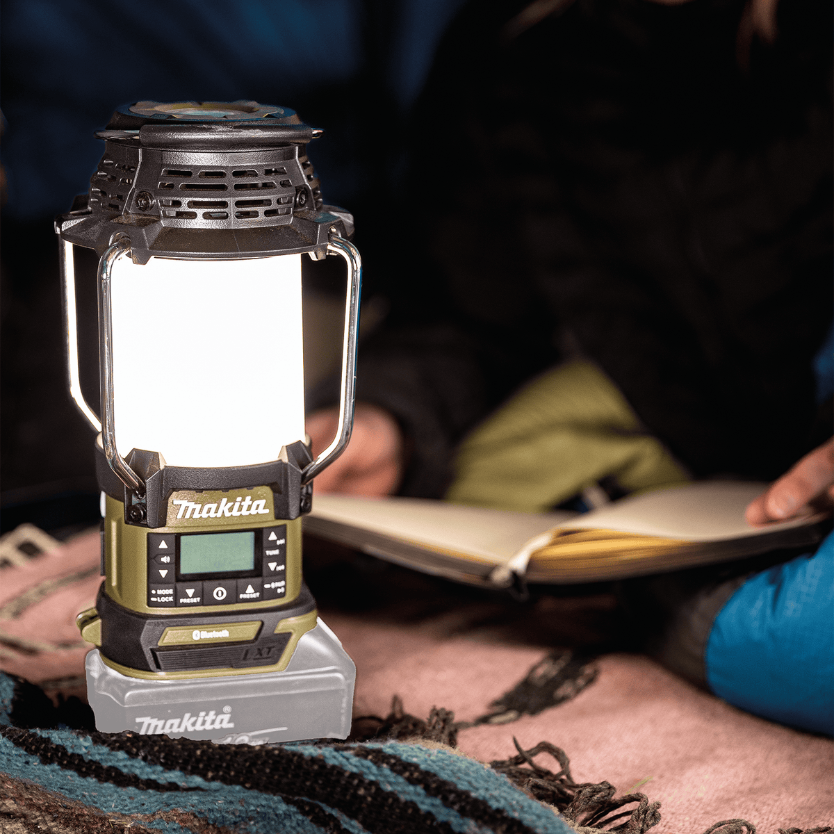 Makita ADRM13 18V LXT lantern illuminating a campsite picnic table to provide warm white light for evening reading.