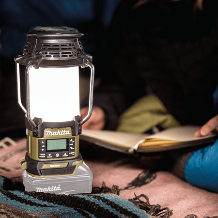 Makita ADRM13 18V LXT lantern illuminating a campsite picnic table to provide warm white light for evening reading.