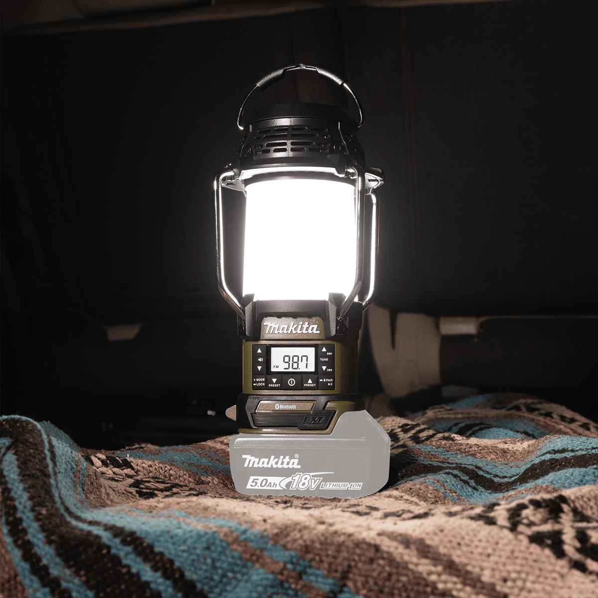 Makita ADRM13 Bluetooth lantern set to FM radio mode displaying 98.7 frequency on its LCD digital control screen.