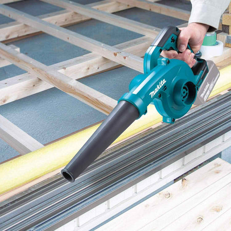 A user holding the cordless blower to clear dust and debris from wooden framing materials on a workbench.