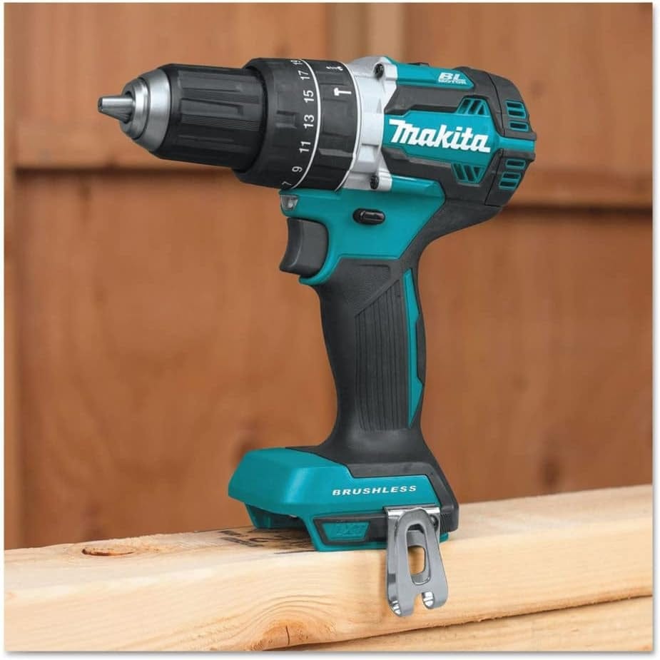 Side profile of the Makita 18V LXT brushless hammer drill resting on a wood beam, highlighting the ergonomic rubber grip, 1/2-inch capacity chuck, and the attached metal belt clip for professional jobsite use.
