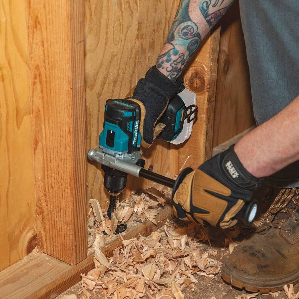 A professional contractor using the Makita XPH14Z hammer driver-drill with an attached side handle to drill through structural floor joists, showcasing the high-torque performance and effective chip clearance.