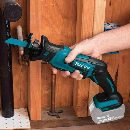 A tradesman using the compact Makita XRJ01Z 18V reciprocating saw to cut a copper pipe in a tight, confined wall cavity for plumbing or HVAC electrical jobs.