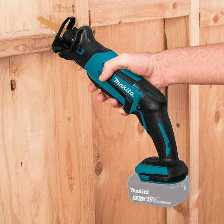 A contractor using the Makita XRJ01Z 18V LXT cordless compact reciprocating saw to perform a precise plunge cut into a wooden wall stud for framing work.