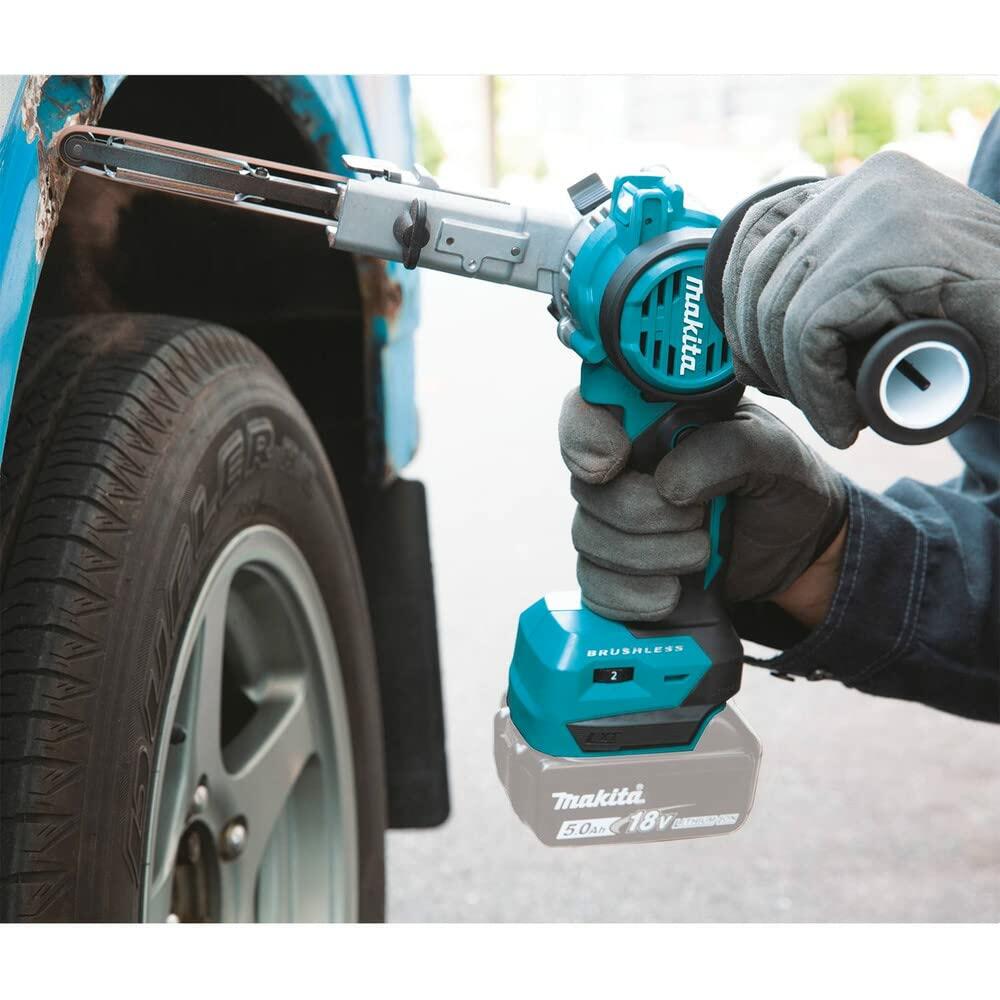 An application shot showing a user wearing gloves using the Makita XSB01Z detail belt sander with a 5.0Ah battery to sand a rusted area on a car's wheel well.