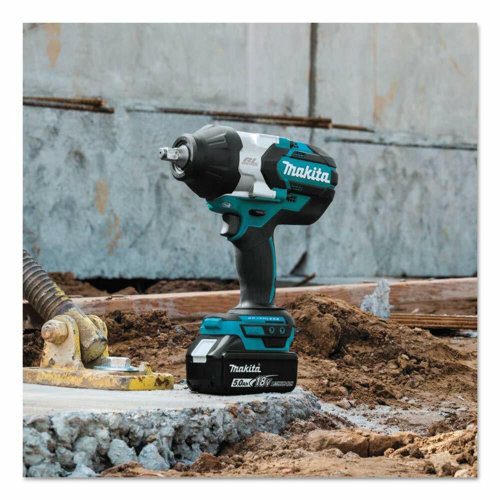 The Makita XWT08T 18V LXT impact wrench with a 5.0Ah battery attached, shown standing upright on a concrete block at a construction site.