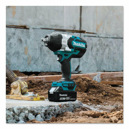 The Makita XWT08T 18V LXT impact wrench with a 5.0Ah battery attached, shown standing upright on a concrete block at a construction site.