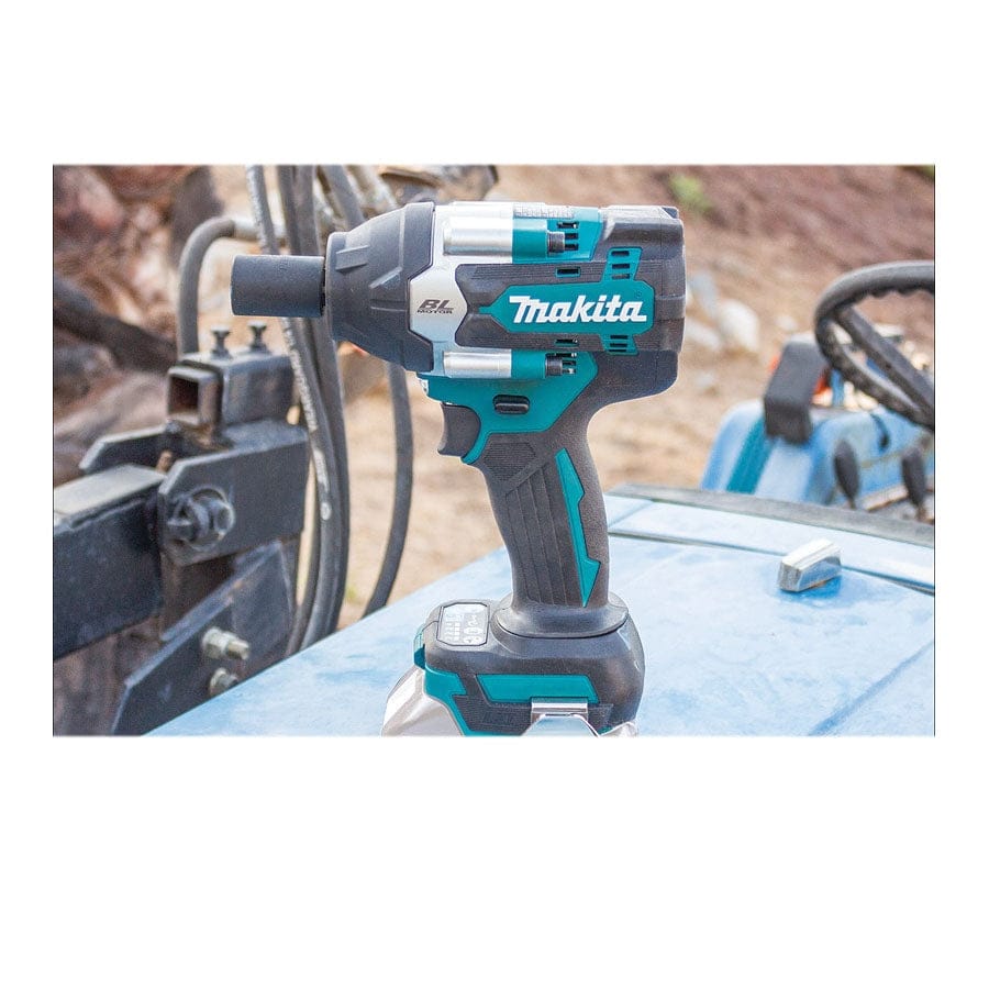 Makita cordless impact wrench resting on blue machinery surface; hydraulic components visible in industrial background.