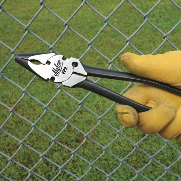 Worker holding Malco FP2 fencing pliers against a chain-link fence to demonstrate field wire cutting, pulling, and tie-wire installation.