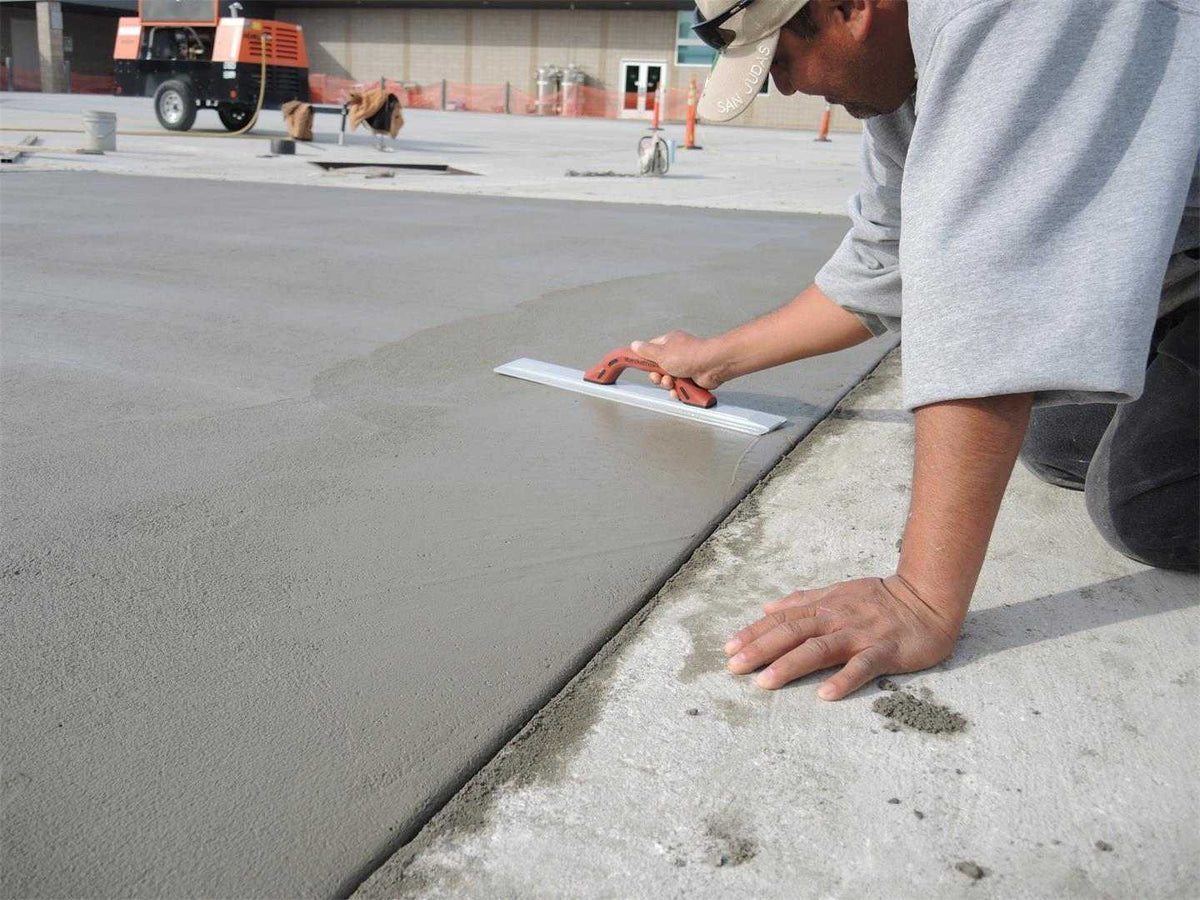 A concrete finisher kneeling on a slab using the Marshalltown magnesium float to smooth the wet surface.