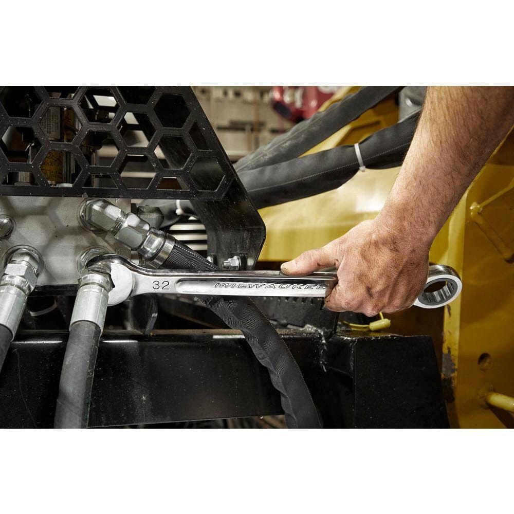 Close-up action shot of a mechanic using a large Milwaukee polished chrome combination wrench on a hydraulic fitting of heavy machinery.