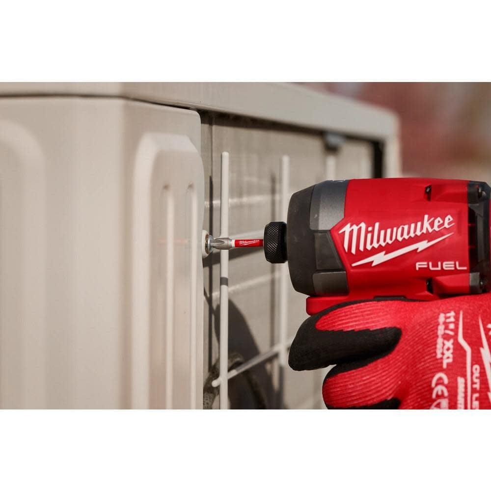 An action shot showing a professional using a red Milwaukee cordless impact driver and a 2-inch SHOCKWAVE Phillips power bit to secure a screw into the side of a white HVAC cabinet.