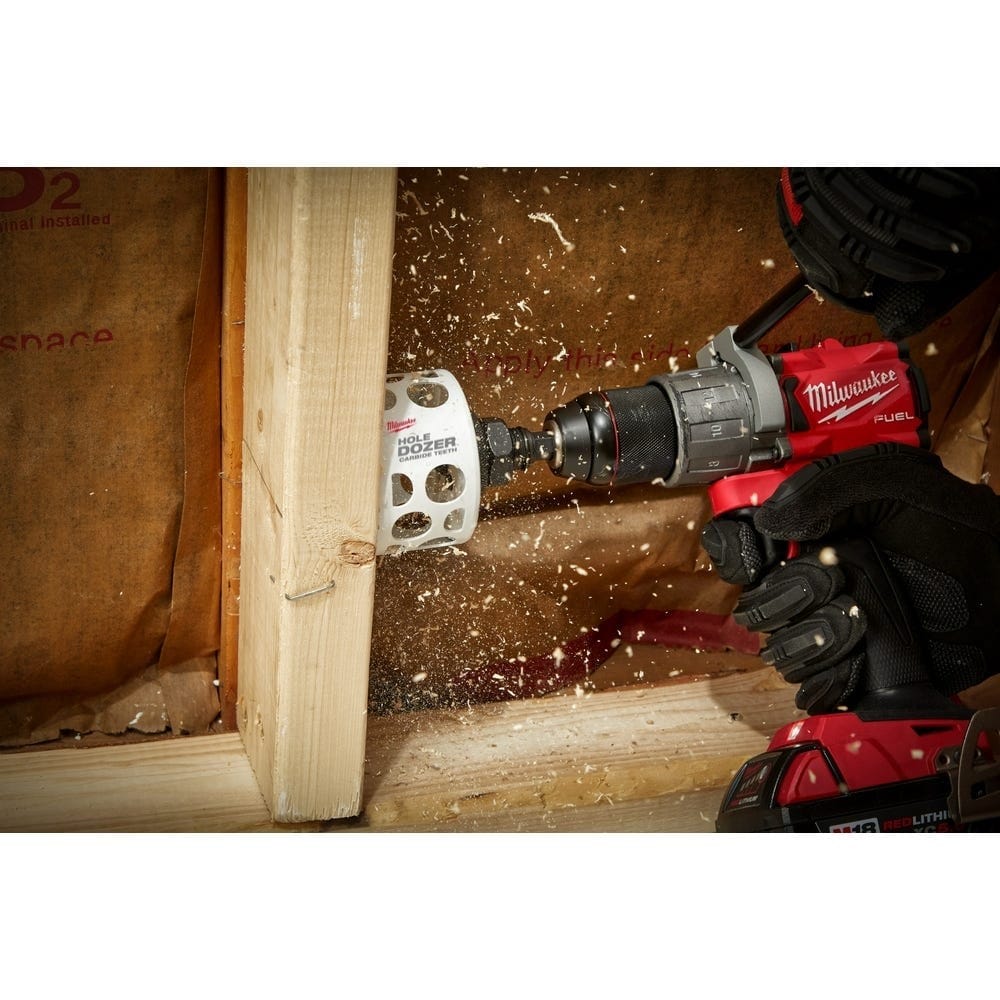 Action shot of a red Milwaukee cordless drill using the white Hole Dozer to cut a clean hole through a wooden wall stud with wood chips flying.