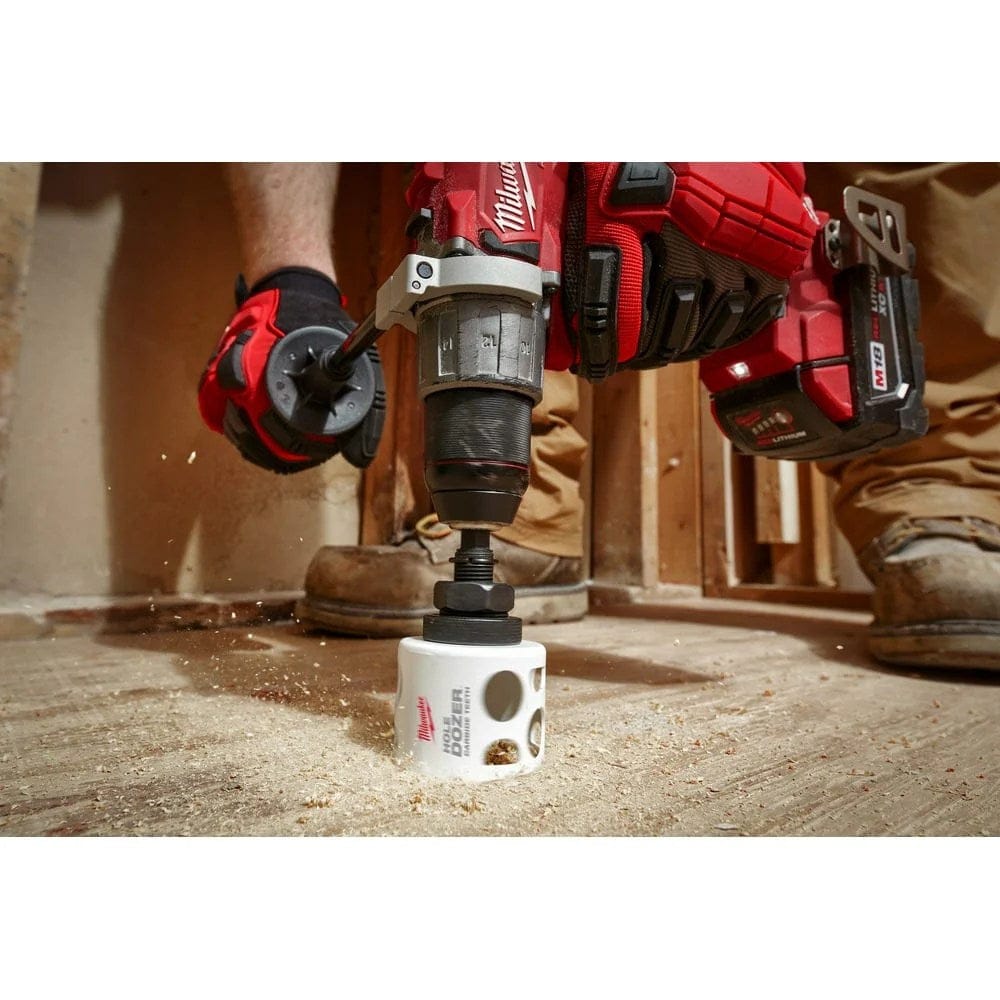Low angle view of a drill equipped with the white hole saw cutting a hole into wooden subflooring.