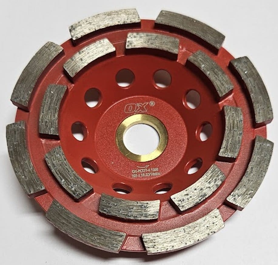 A top-down view of the OX Tools 4-inch double row diamond cup grinder featuring a red steel body with two concentric rows of aggressive segmented diamond teeth for rapid concrete and masonry surface preparation.