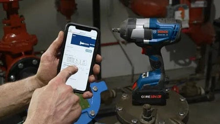 Person holding a smartphone in front of a Bosch cordless impact wrench, displaying a connected app interface for tool configuration and diagnostics