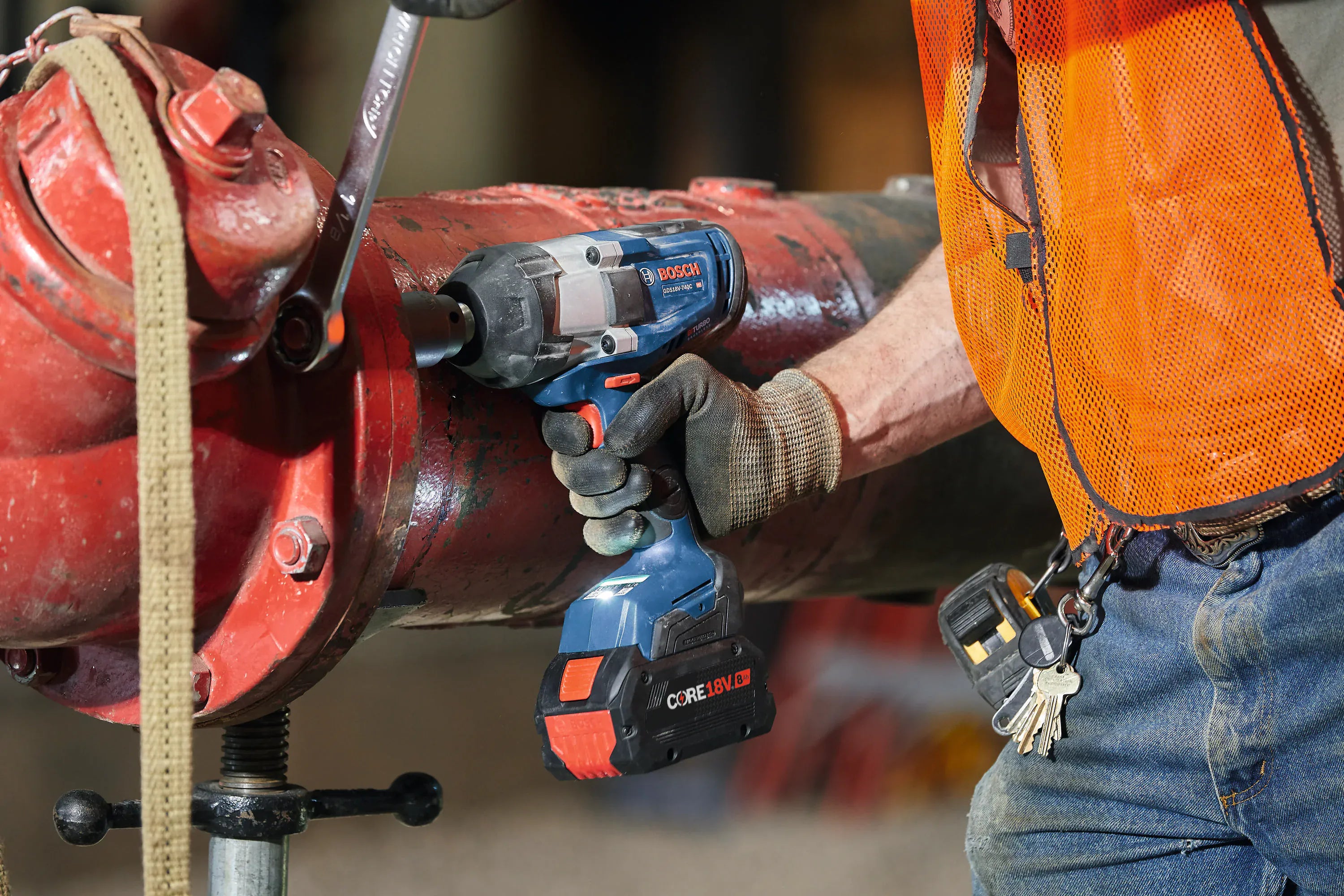 A close-up application shot of a technician using the Bosch BITURBO brushless impact wrench powered by a CORE18V battery pack to tighten mechanical pipe flange bolts in a commercial setting.