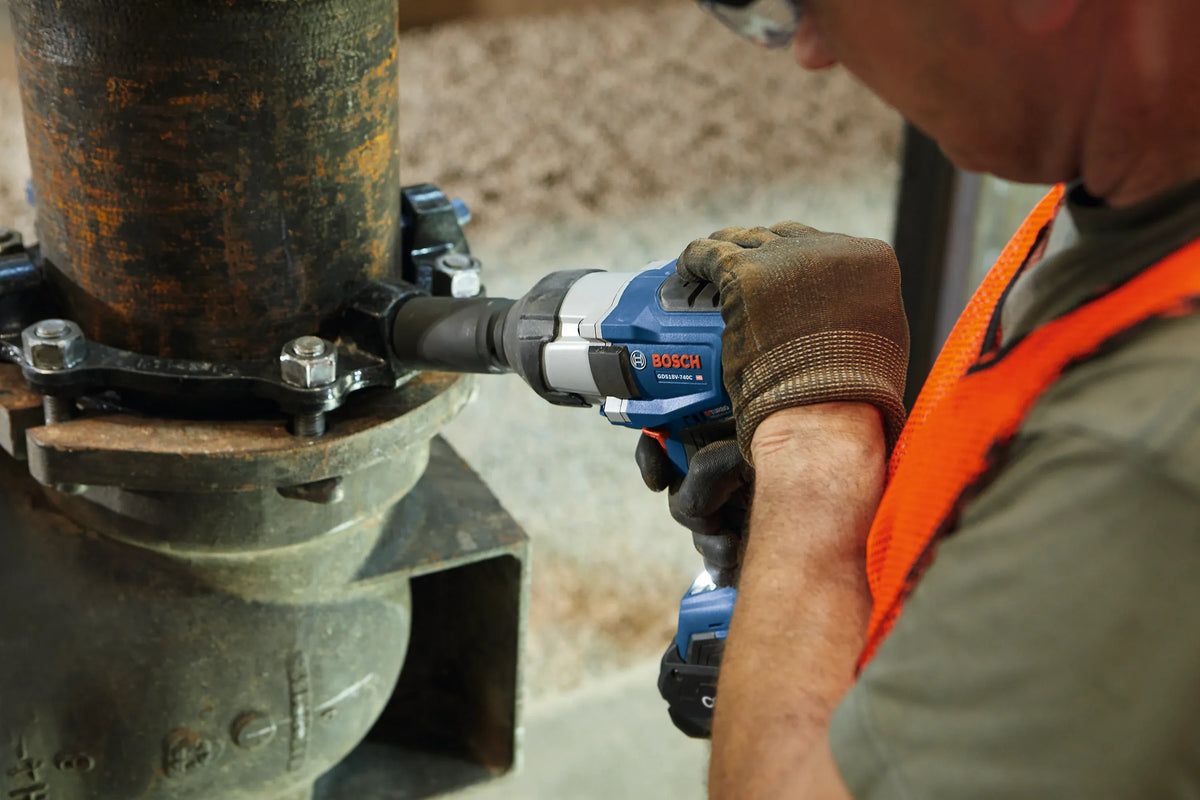 A high-angle view of a worker using the Bosch high torque cordless impact wrench with a deep impact socket engaged on an industrial mechanical pipe coupling connection.