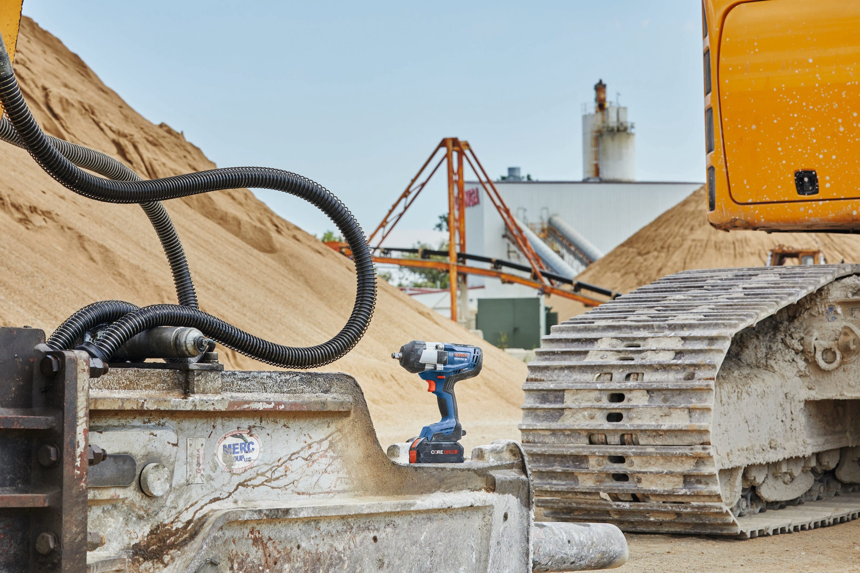 An industrial outdoor application shot of the Bosch PROFACTOR 18V impact wrench sitting on top of a heavy-duty yellow construction excavator bucket at a sand and gravel facility.