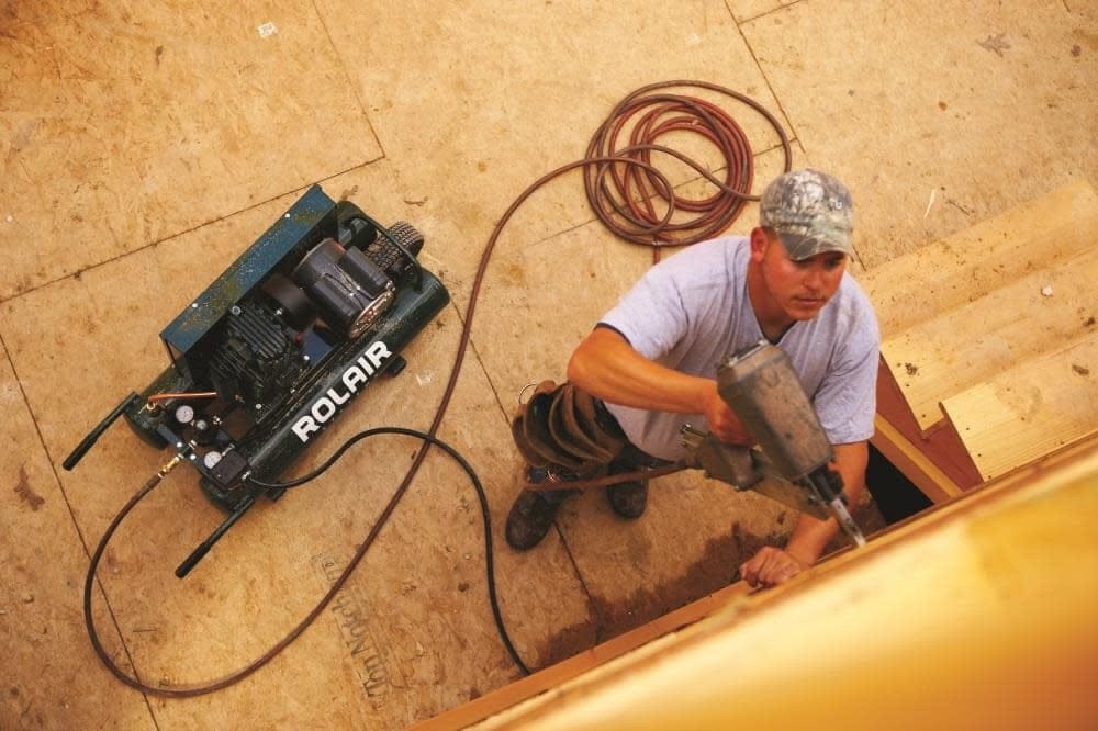Overhead action shot of a construction worker using a pneumatic framing nailer supplied by the portable Rolair twin tank wheelbarrow compressor on a jobsite floor