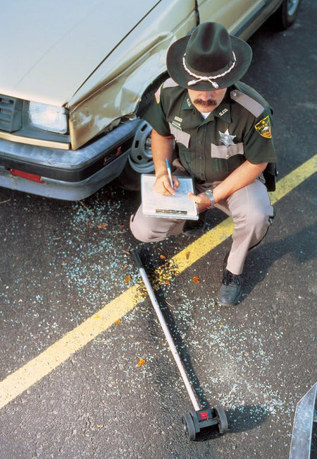 Law enforcement officer using a Rolatape 32-112 dual wheel measuring wheel to record precise distance metrics at a roadway vehicle accident scene.