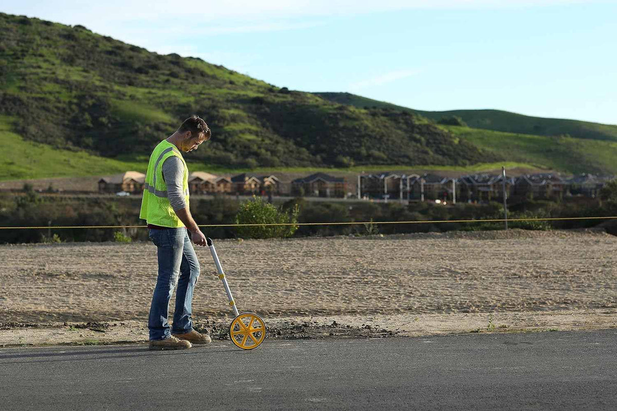 A professional using the Rolatape RT300 measuring wheel on an asphalt surface at a construction site, demonstrating its accuracy and ease of use in outdoor surveying and property estimation.