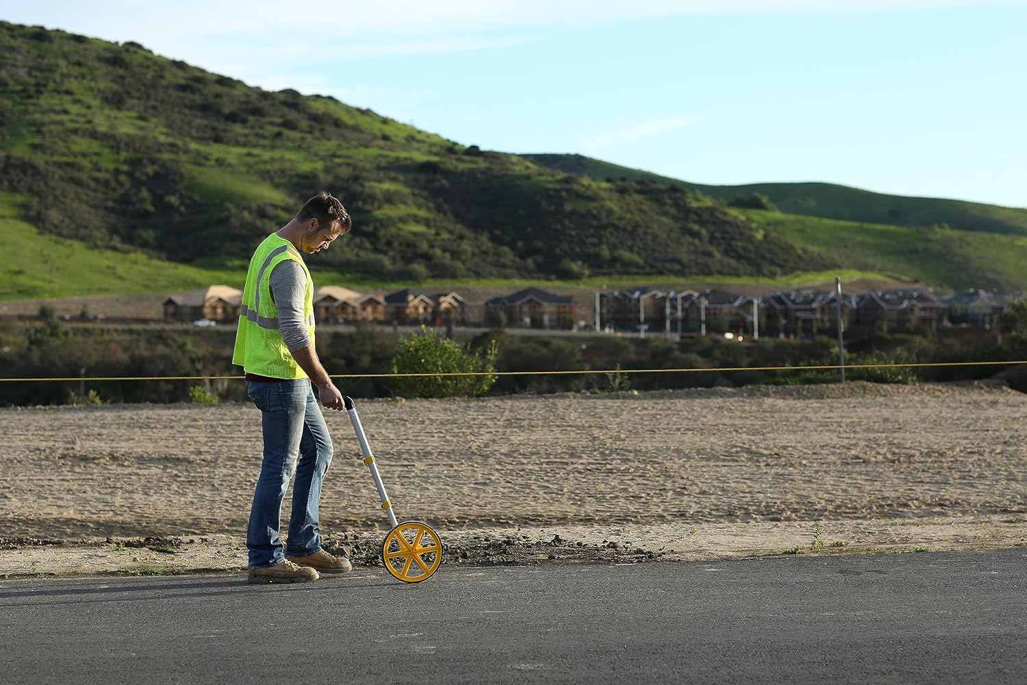 A professional using the Rolatape RT300 measuring wheel on an asphalt surface at a construction site, demonstrating its accuracy and ease of use in outdoor surveying and property estimation.
