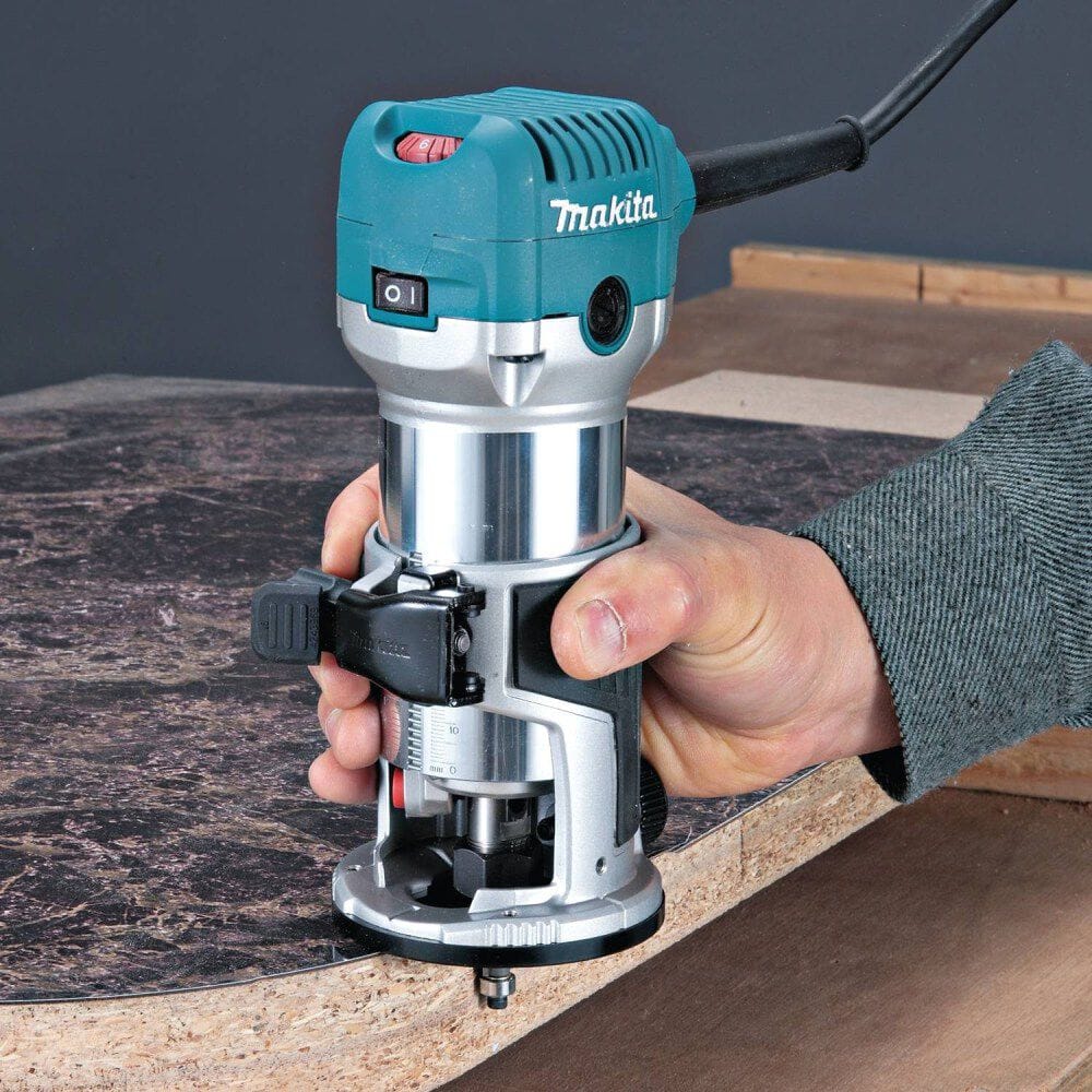 A user routing the edge of a dark laminate countertop board with the Makita RT0701C 6.5 Amp variable speed compact router, demonstrating precise control and comfortable one-handed operation.
