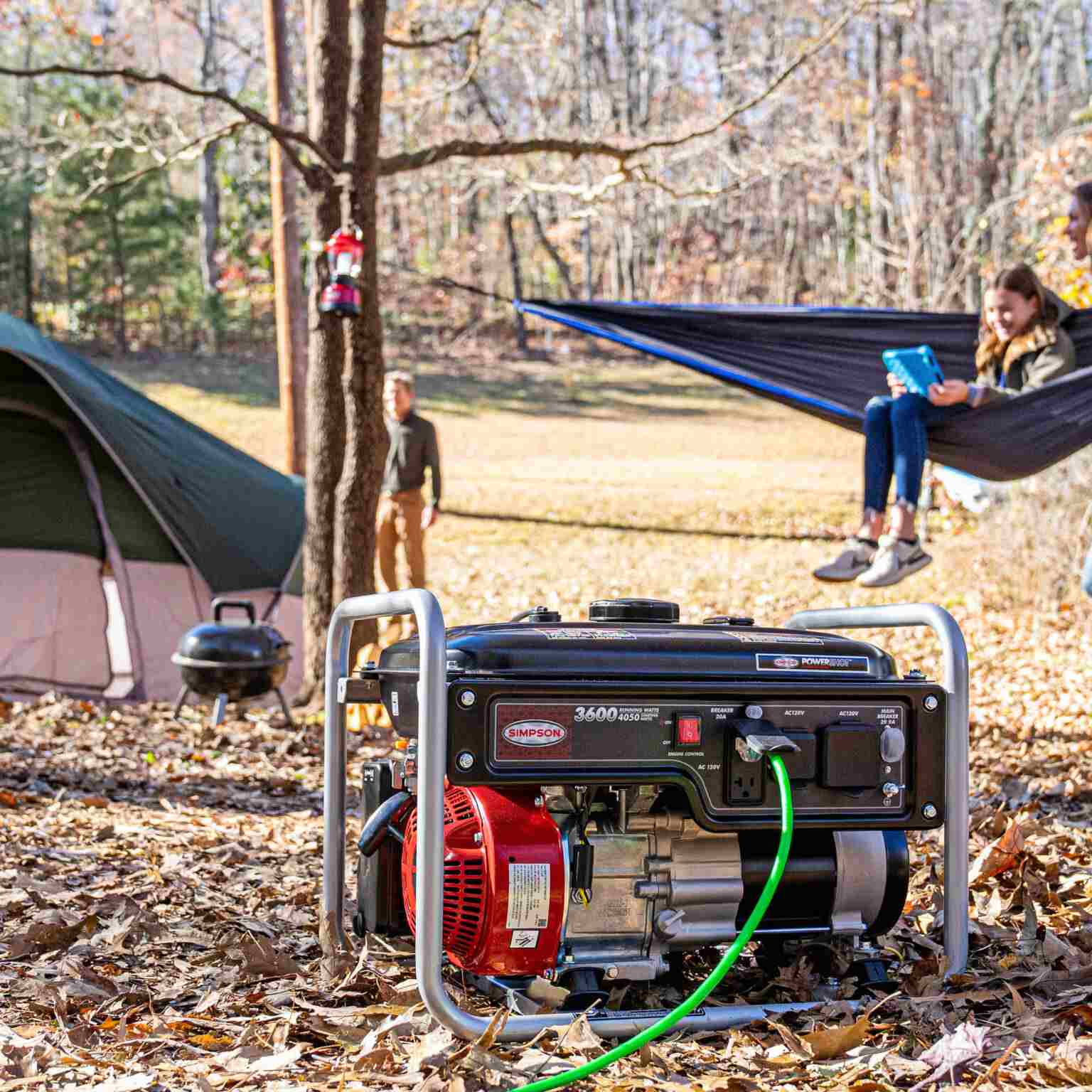 Lifestyle image showing the portable generator set up at a campsite with a tent and people relaxing in hammocks in the background.