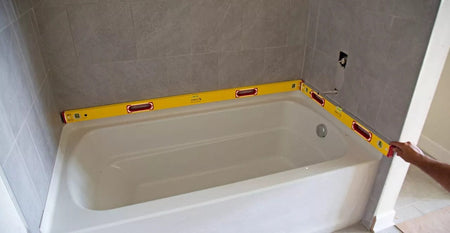A worker holding the long 58-inch STABILA spirit level horizontally against a freshly tiled bathroom wall to check for levelness.