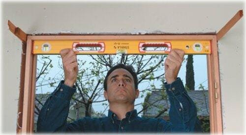 A worker holding the 48-inch STABILA level horizontally across the top frame of a rough window opening to check for levelness during construction.