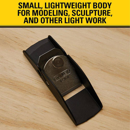 Top down view of the compact STANLEY 12-101 trimming plane resting on a light wood work surface beneath an informational banner explaining its utility for modeling, sculpture, and light craft applications.